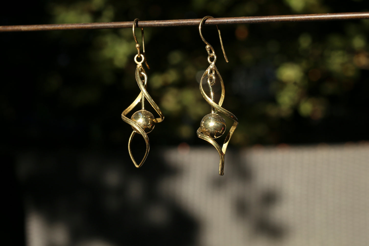 brass earrings hanging on a wire with a blurred natural background