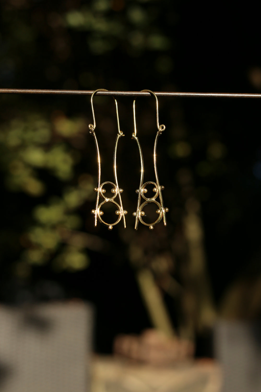brass earrings hanging on a dark surface with a blurred natural background