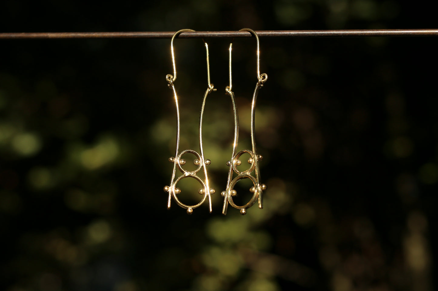 brass earrings hanging on a wire against a blurred natural background
