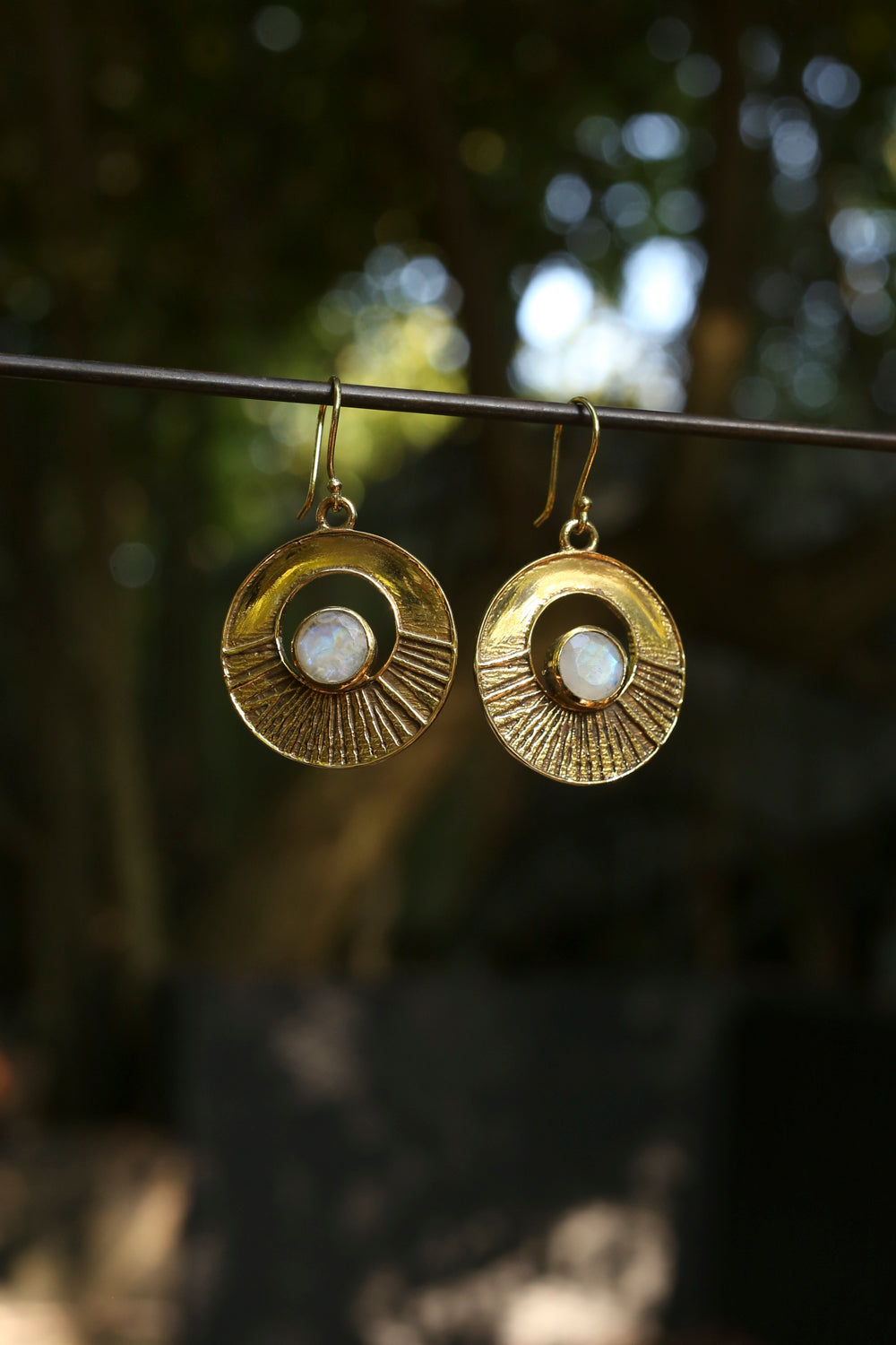 brass earrings with a moonstone hanging on a wire against a blurred natural background