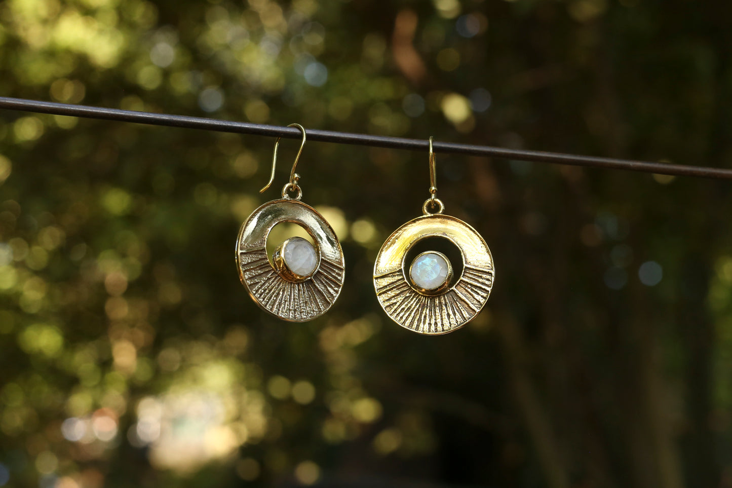 brass earrings with a moonstone against a blurred natural background