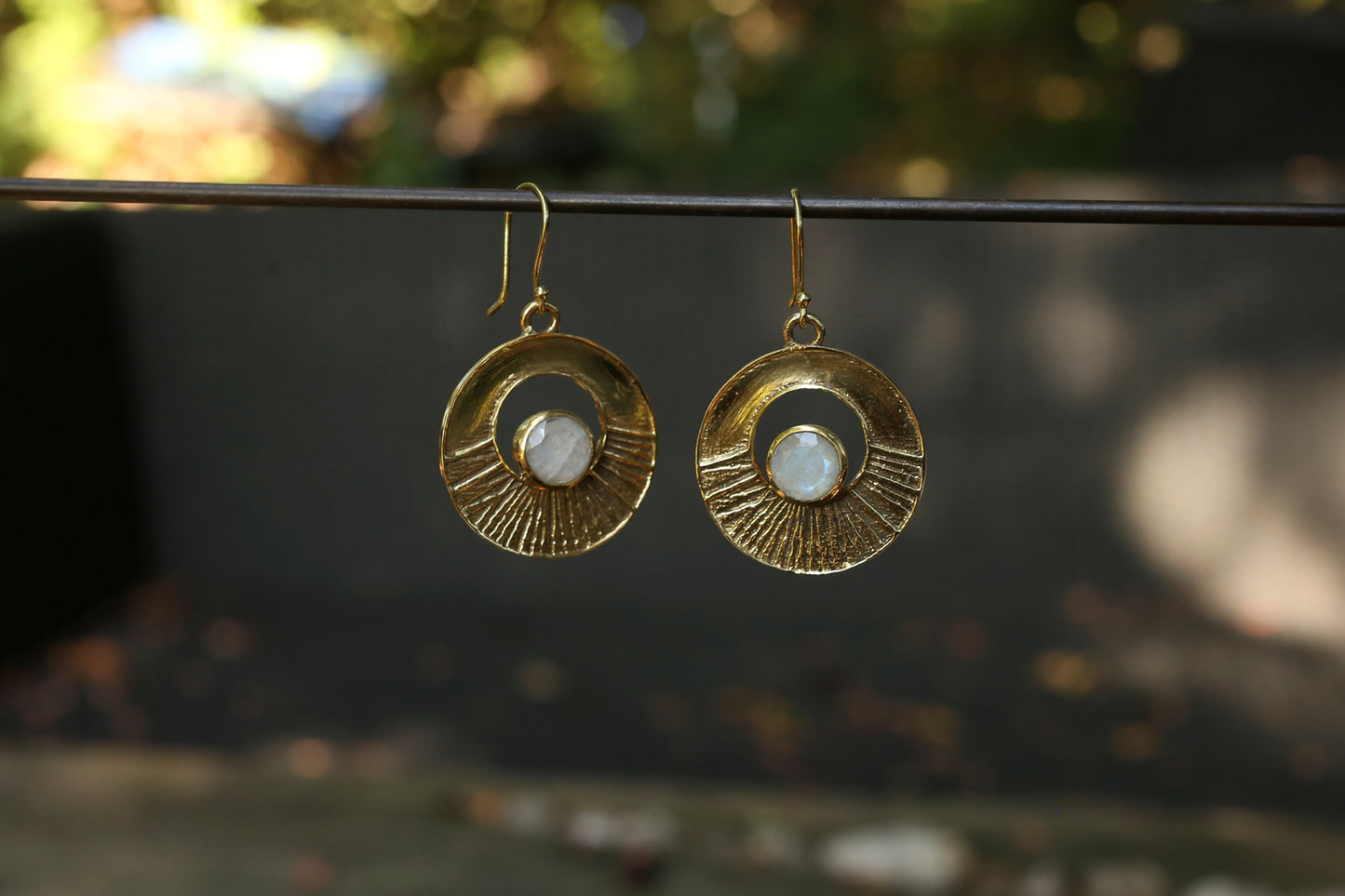 brass earrings with a moonstone on a dark surface with a blurred natural background