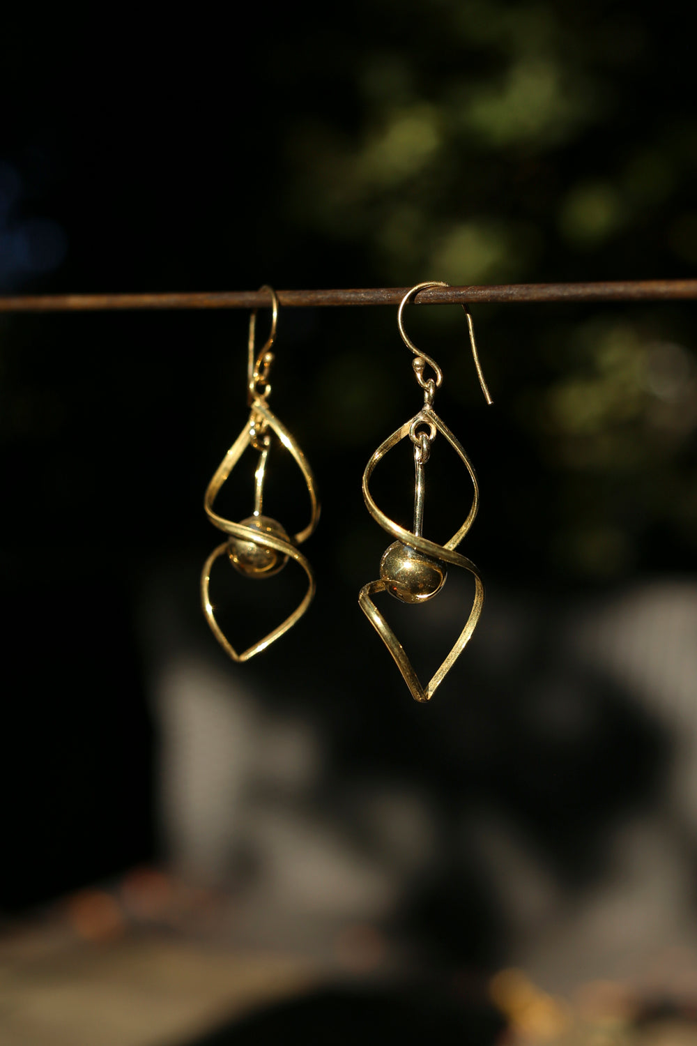brass earrings hanging on a branch with a blurred natural background