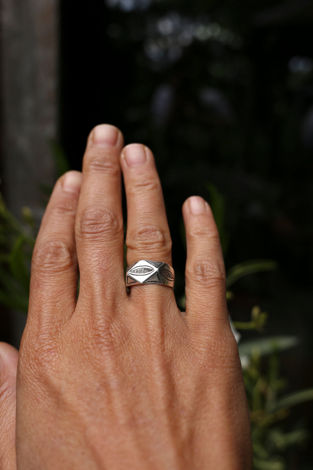 Hand wearing a ring with a diamond-shaped design against a dark background