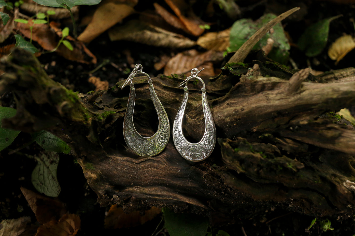 Silver hoop earrings on a wooden surface with a natural background