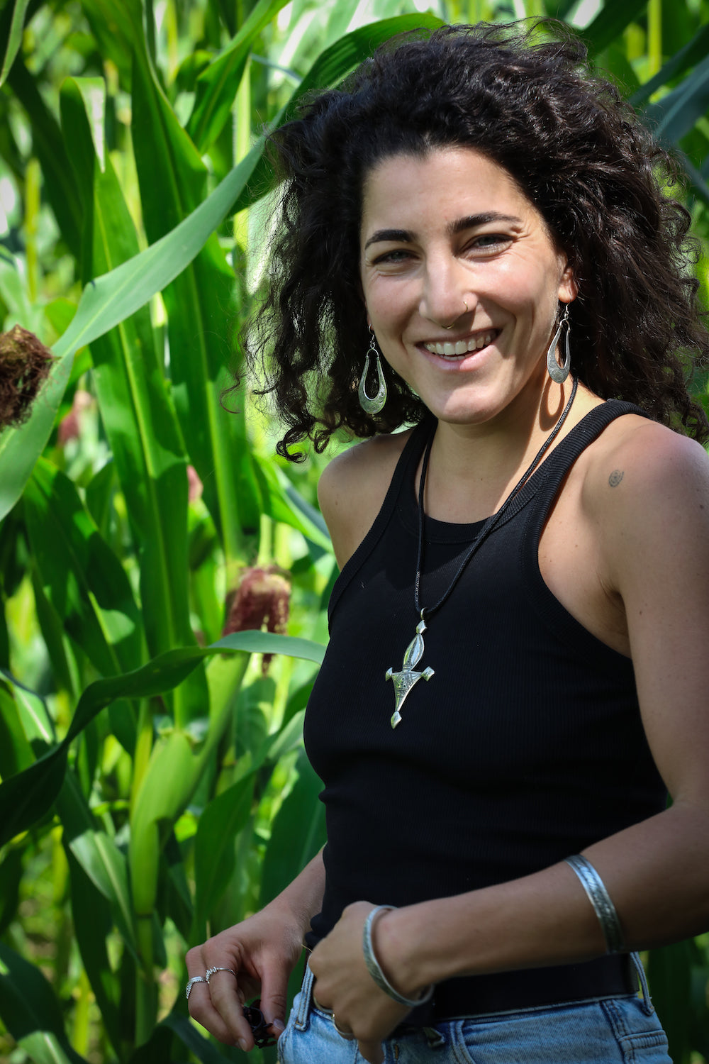 Woman standing in a cornfield wearing a black tank top and blue jeans.