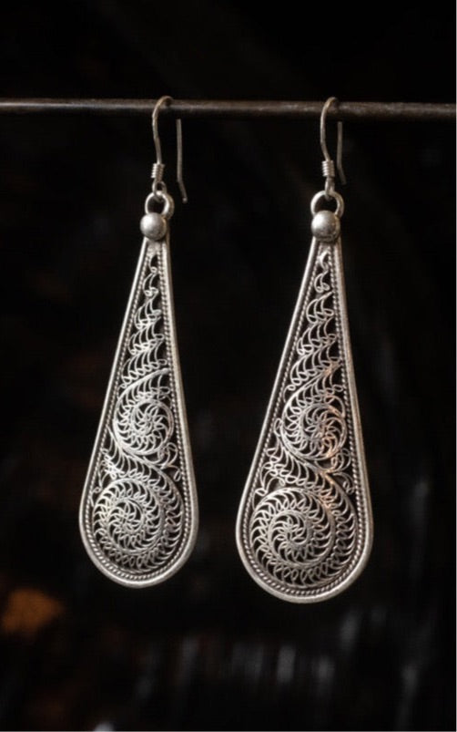 Silver Newari earrings with intricate traditional Nepalese filigree design hanging on a rod