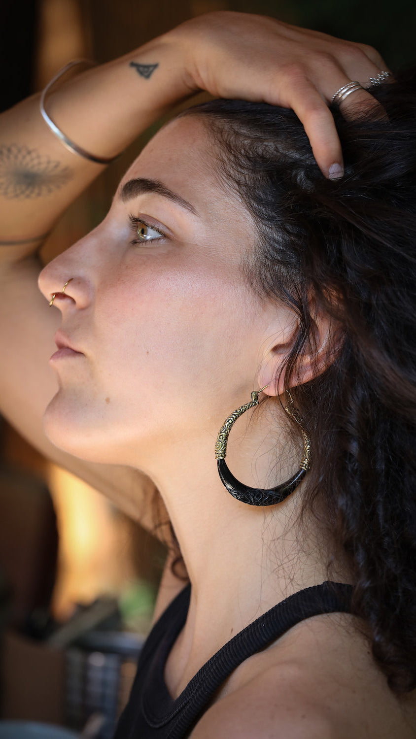 Woman with hoop earrings and tattoos on her arm, looking away from the camera.