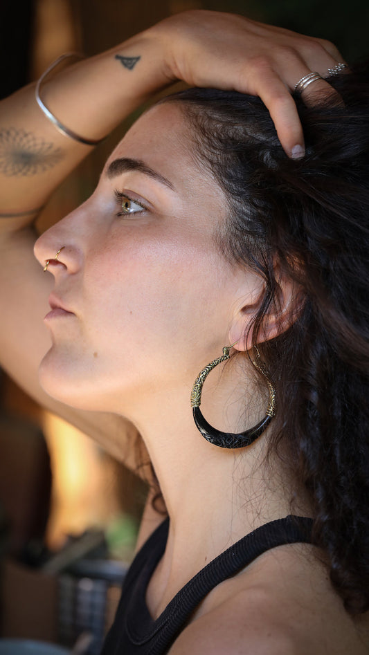 Woman with hoop earrings and tattoos on her arm, looking away from the camera.
