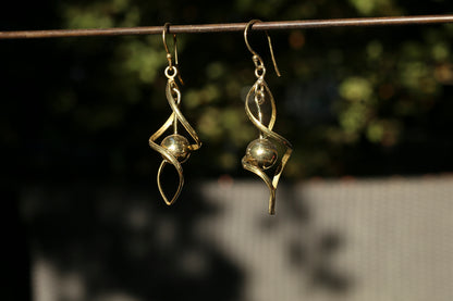 brass earrings hanging on a wire with a blurred natural background