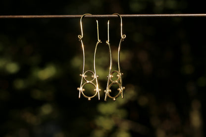 brass earrings hanging on a wire against a blurred natural background