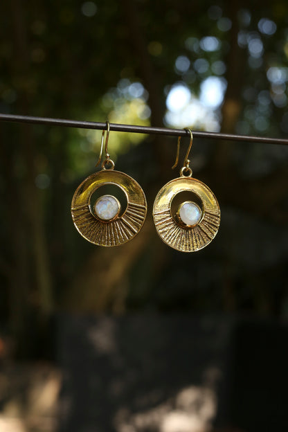 brass earrings with a moonstone hanging on a wire against a blurred natural background