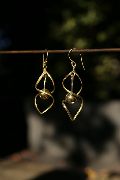 brass earrings hanging on a branch with a blurred natural background