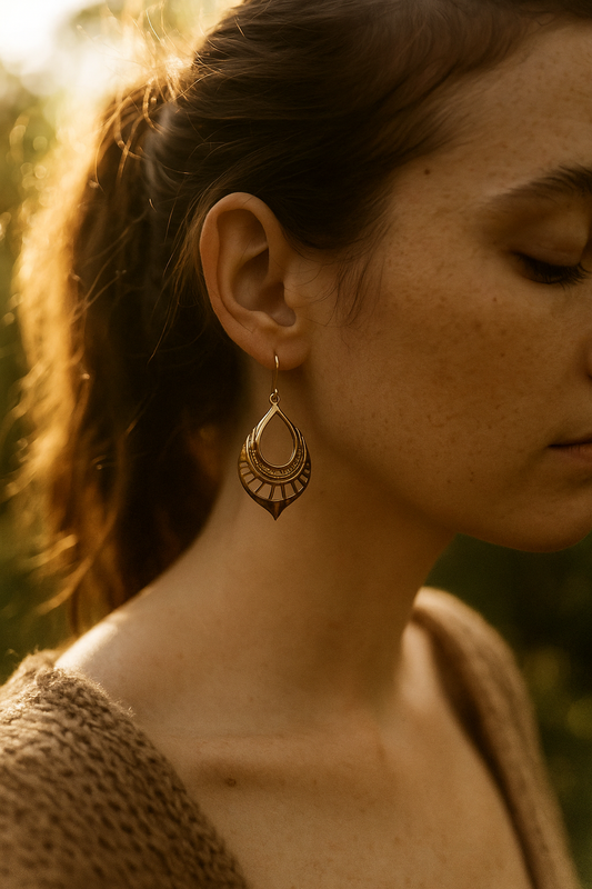 Close-up of a woman wearing brass earrings with a blurred natural background