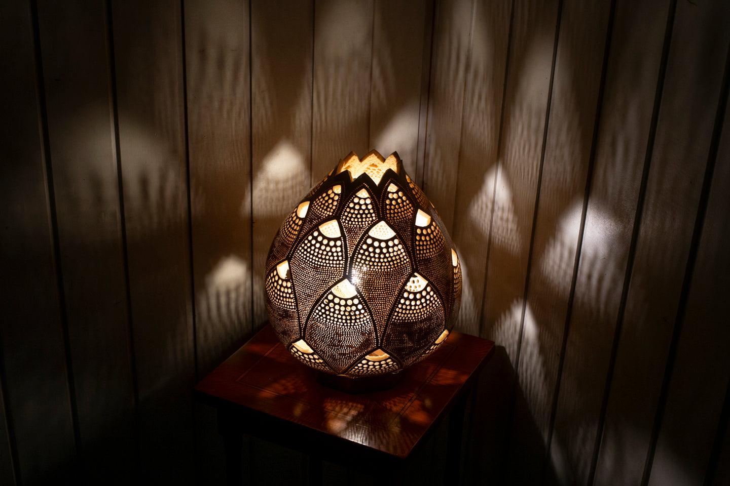 Image of a handcrafted calabash lamp. The gourd's surface is intricately carved with patterns that allow soft light to shine through, creating a warm and inviting ambiance. The lamp is a blend of natural elegance and artistry, casting gentle shadows that enhance its beauty