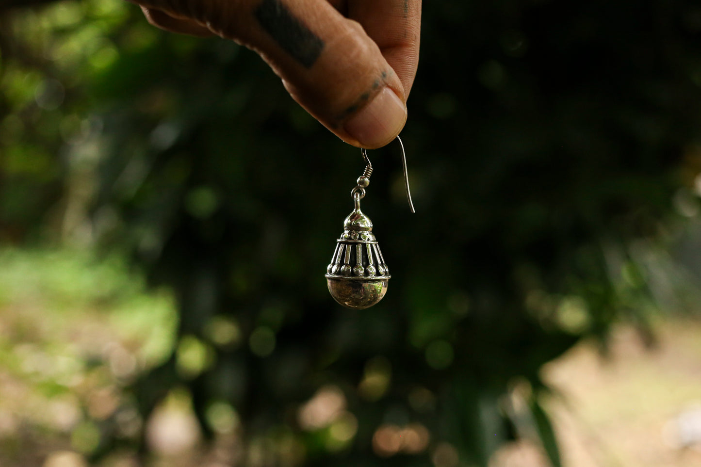 Silver earring held by a hand against a blurred natural background