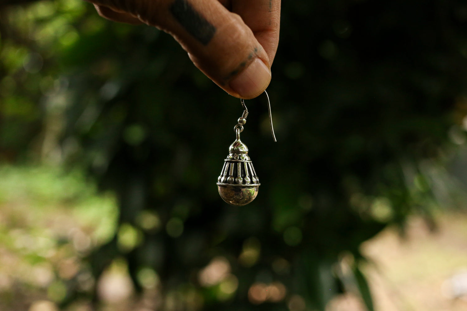 Silver earring held by a hand against a blurred natural background