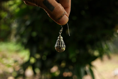 Silver earring held by a hand against a blurred natural background