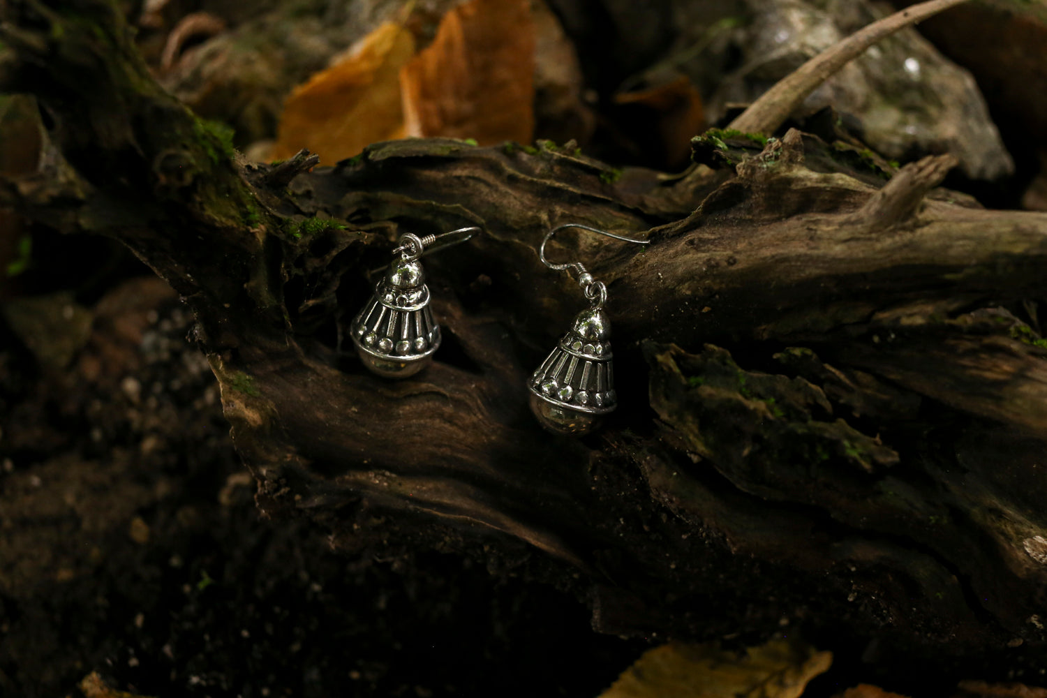 Silver bell-shaped earrings on a textured wooden surface