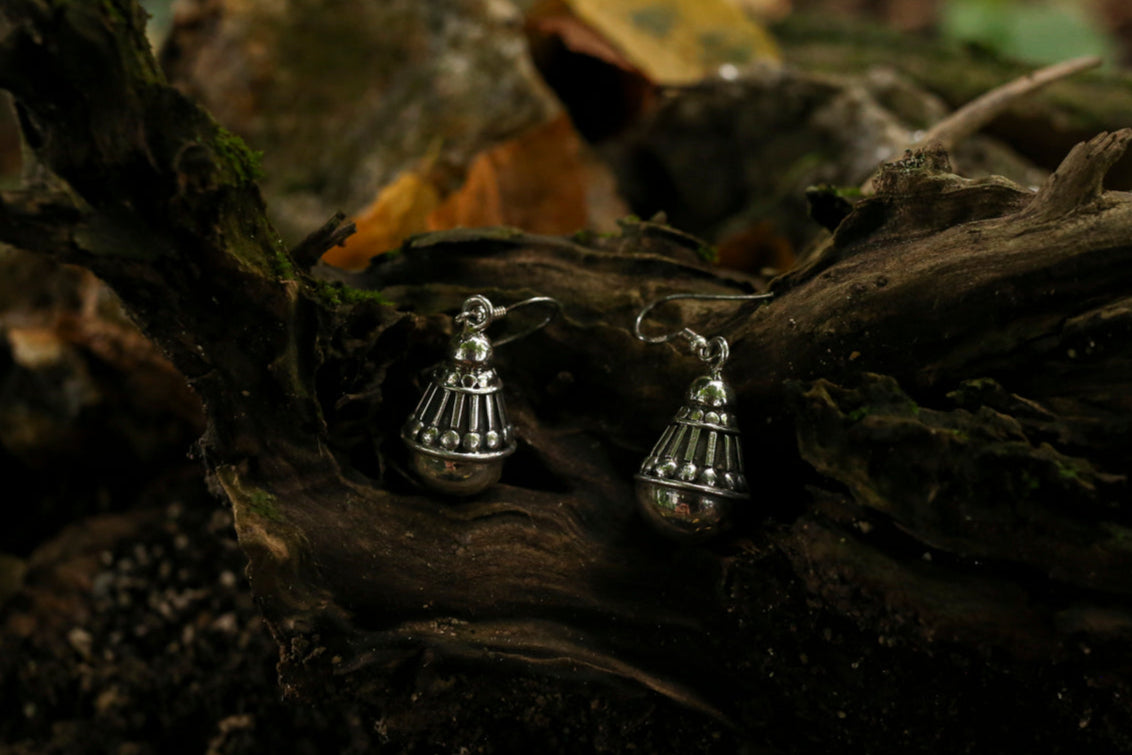 Silver bell-shaped earrings on a textured wooden surface