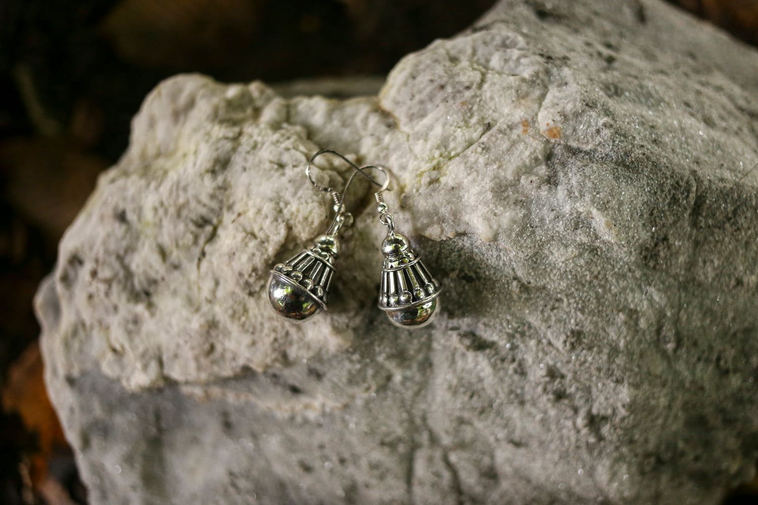 Silver earrings with dangling balls on a textured stone surface