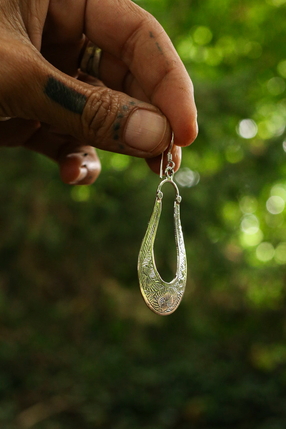 Hand holding a silver earring with a blurred green background