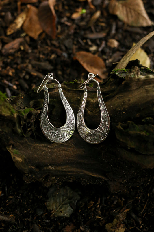 Pair of silver earrings on a wooden surface with leaves in the background