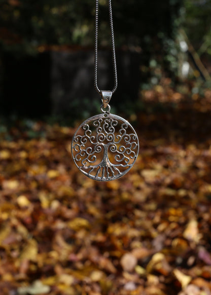 Silver tree of life pendant hanging against a natural background with autumn leaves